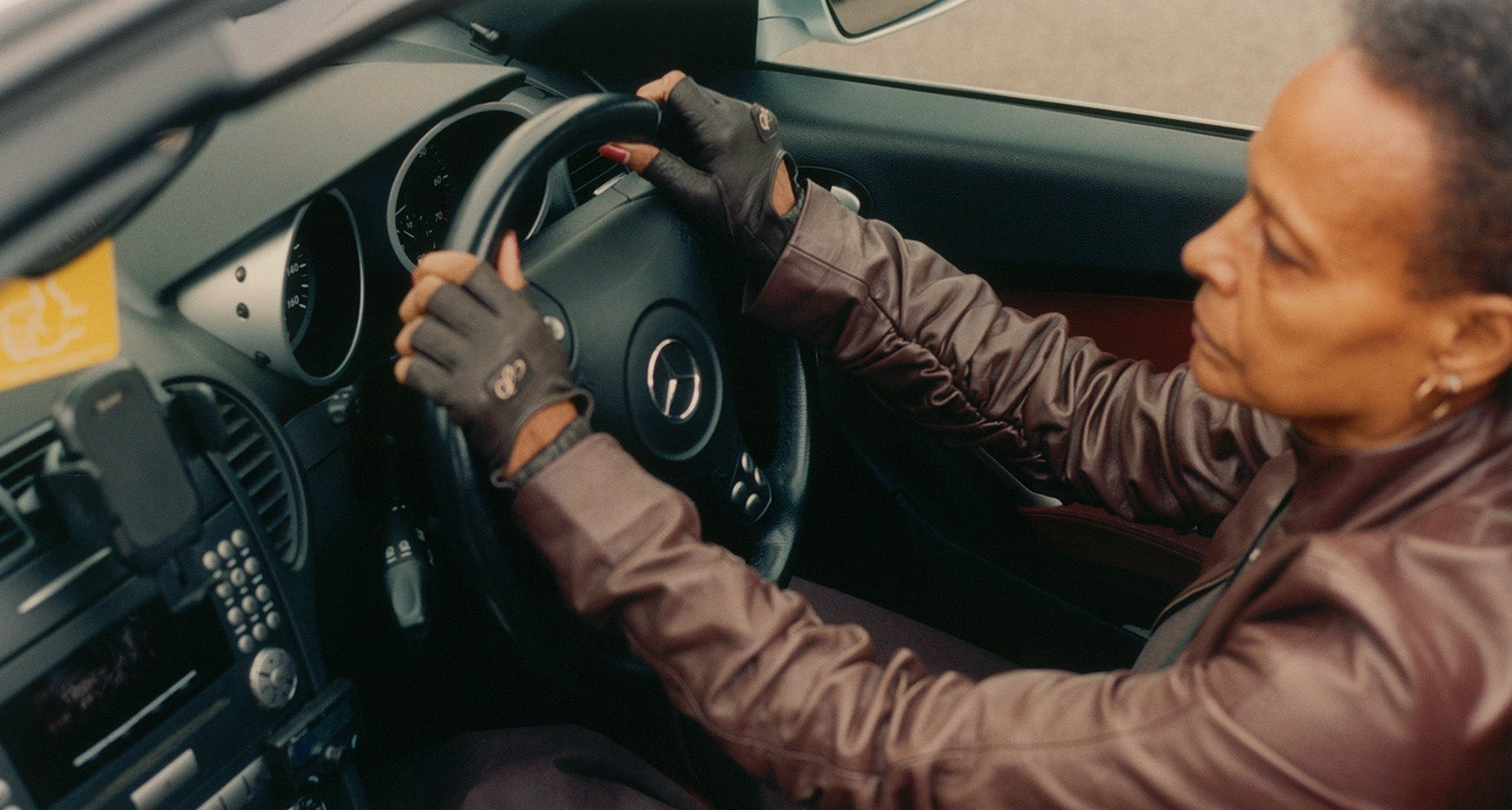 Person driving a car with a focus on the steering wheel and dashboard.